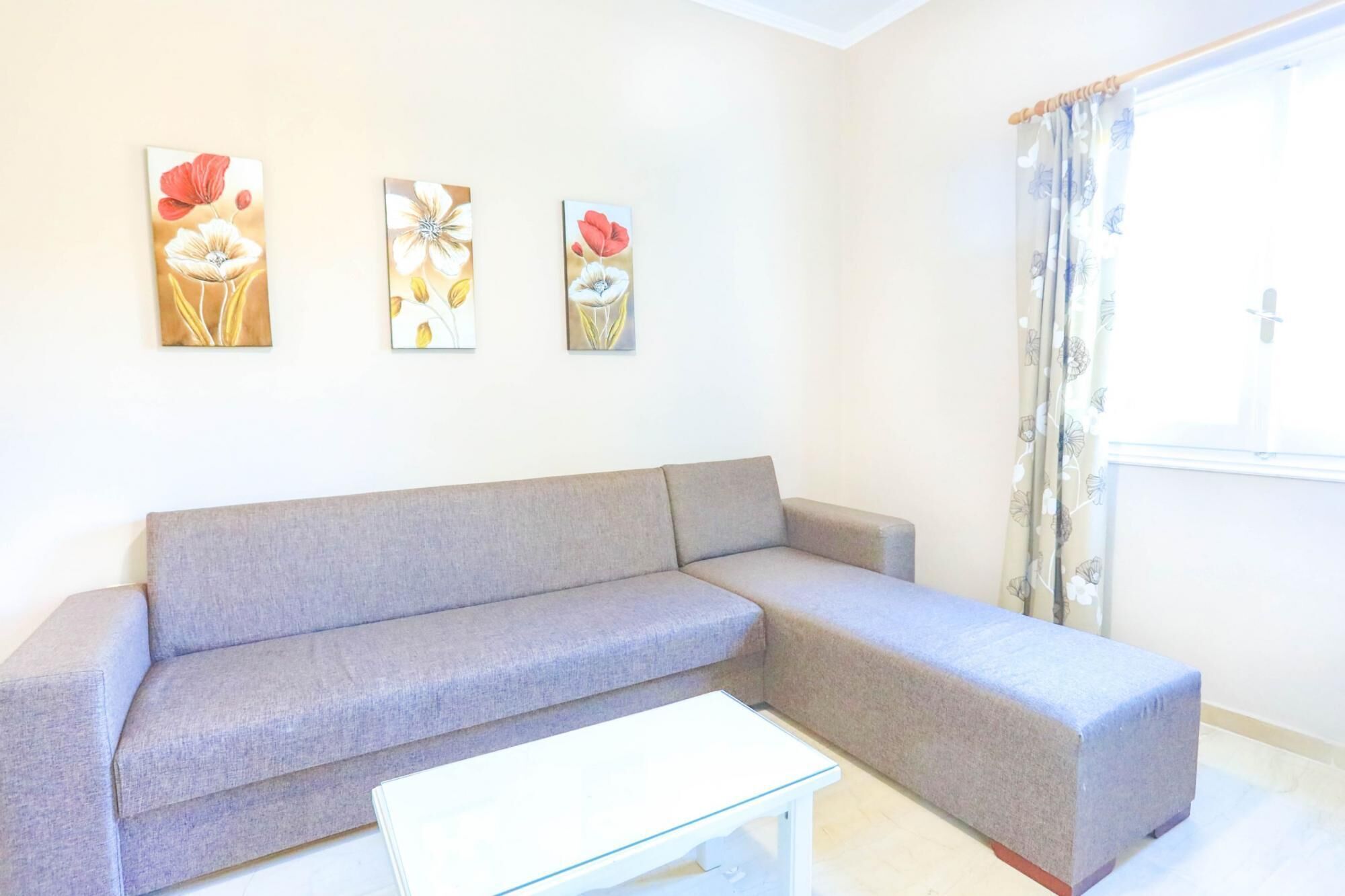 Una sala de estar con un sofá gris, una mesa de centro blanca y tres cuadros florales en la pared.