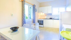 A compact kitchen with white cabinets, a stove, and a sink. There's a dining table with chairs and a bowl on it.
