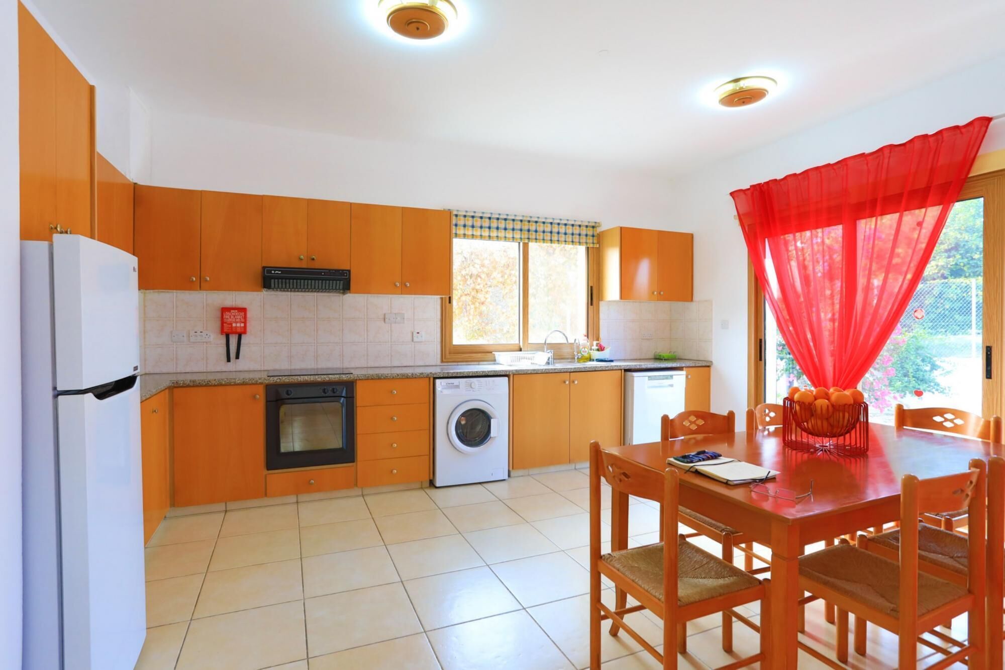 A kitchen with orange cabinets, a white refrigerator, a washing machine, and a dining area with a table and chairs.