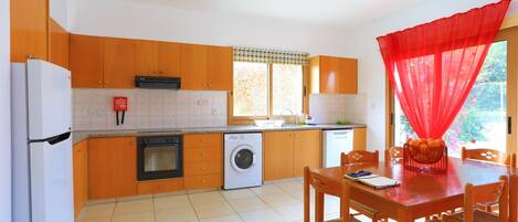 A kitchen with orange cabinets, a white refrigerator, a washing machine, and a dining area with a table and chairs.