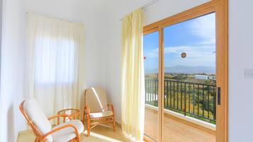 A balcony with wicker chairs, a view of a landscape with mountains, and a clear sky.