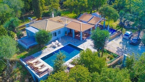 A large house with a swimming pool, multiple outdoor seating areas, and a garage with two cars. - Achilleion Forest Villa (Corfu)