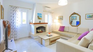 A living room with a fireplace, sofa, and coffee table. - Achilleion Forest Villa (Corfu)