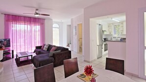 A modern living room with a sofa, coffee table, and dining table. There is a kitchen visible through an open door. - Villa Irina Polis in Polis (Polis)