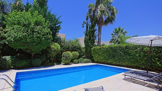 A swimming pool with lounge chairs and an umbrella, surrounded by lush greenery and palm trees. - Villa Irina Polis in Polis (Polis)