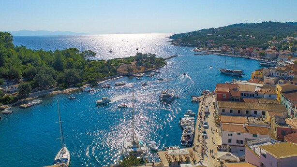 A coastal town with boats docked along the marina, buildings with red-tiled roofs, and a clear view of the sea. - Villa Eleni Paxos in Gaios (Paxos)