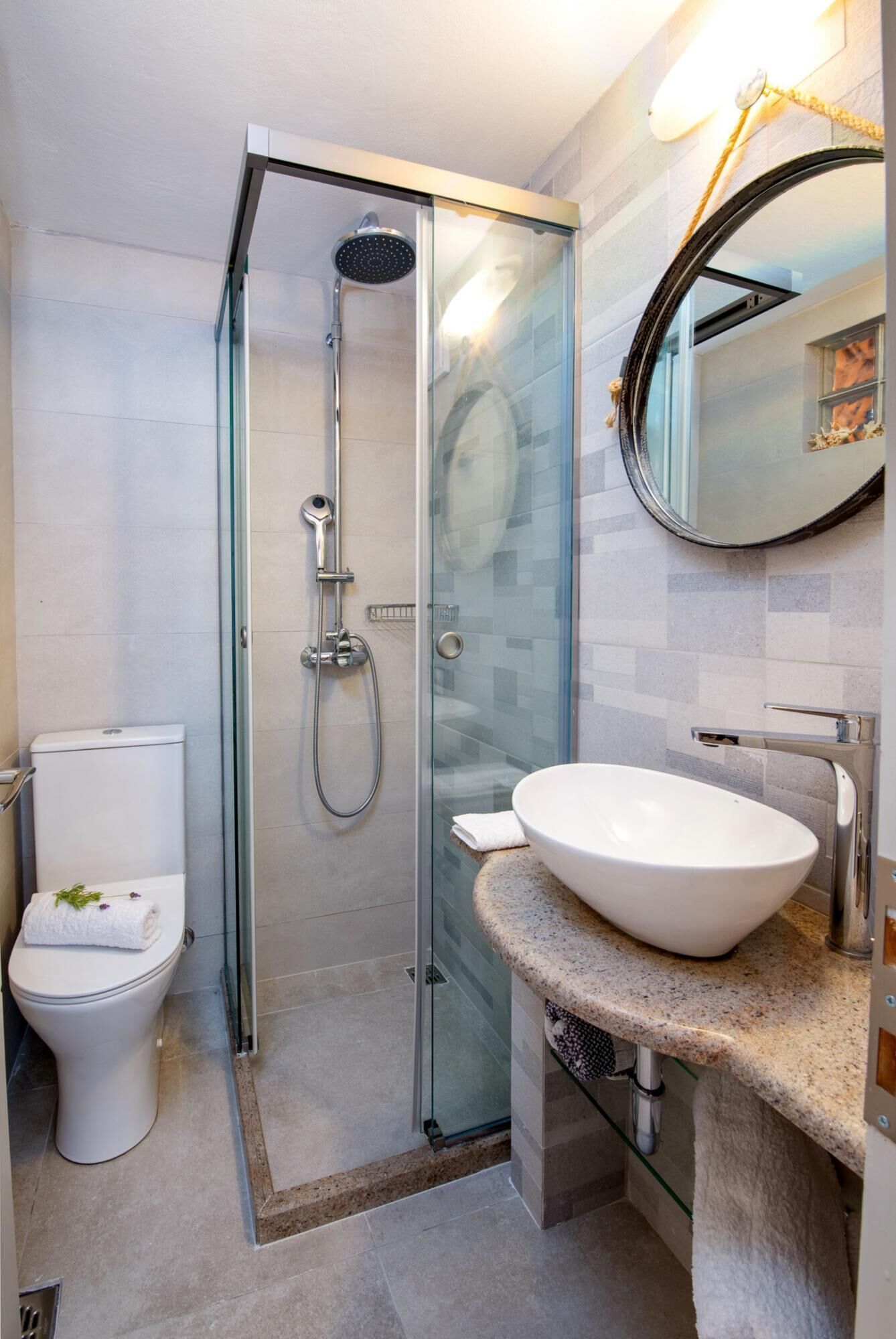 A modern bathroom with a glass-enclosed shower, a white toilet, and a granite countertop with a sink.