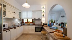 A modern kitchen with white cabinetry, a built-in oven, a coffee maker, and a wooden island with bread and pastries. - Villa Eleni Paxos in Gaios (Paxos)