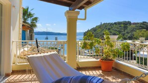 A balcony with a white chair, a potted plant, and a view of the sea and hills. - Paola House in (Corfu)