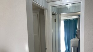 A hallway with a white door leading to a bathroom with a blue shower curtain and a small trash bin.
