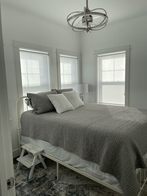 A bedroom with a bed, a nightstand, a step stool, and a ceiling fan.