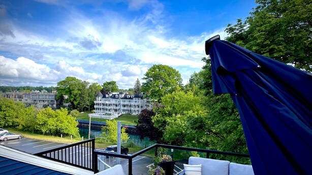 A balcony with outdoor seating, a view of a lake, and a building in the background. - Riverwalk One Condo with rooftop deck (Charlevoix)