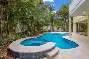Una piscina con idromassaggio, circondata da piante tropicali e una zona patio coperta.