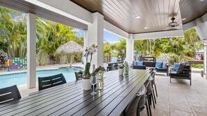 Un espacio al aire libre techado con piscina, sillas de descanso y una mesa de comedor.