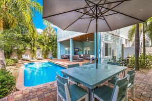 Zona junto a la piscina con mesa y sillas, un espacio de estar techado y piscina.