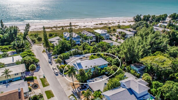Vue aérienne d’une zone résidentielle côtière, avec des maisons, une plage et un ciel dégagé.
