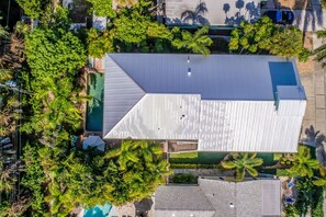 Vista aérea de un edificio moderno con techo inclinado, rodeado de exuberante vegetación y una piscina.