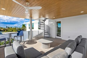 A modern outdoor living area with a wooden ceiling, a spiral staircase, a round table, and a gray sofa. - Beach Walk: Ultimate Luxury! Games Galore, Pool, Spa Rooftop Deck (Holmes Beach)