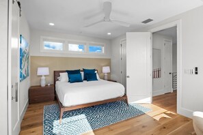 A modern bedroom with a wooden bed, a ceiling fan, and a large window. - Beach Walk: Ultimate Luxury! Games Galore, Pool, Spa Rooftop Deck (Holmes Beach)
