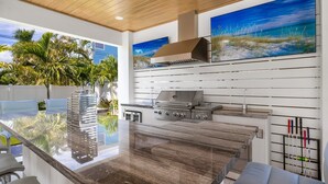 Una cucina moderna con una grande isola, elettrodomestici in acciaio inossidabile e vista su una zona esterna tropicale.