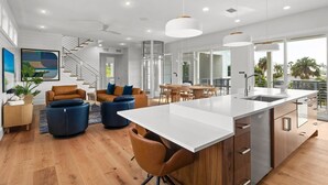 Una cucina moderna con un'isola grande, pavimento in legno e una zona pranzo con una scala che porta a un balcone.