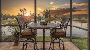 Un balcón con una mesa redonda y dos sillas, con vistas al agua y a un atardecer.