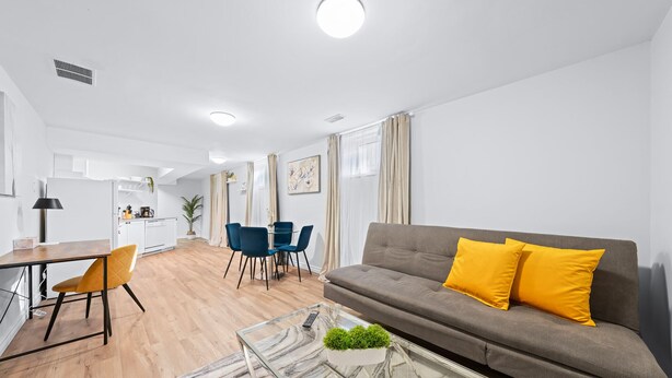 A modern living room with a grey sofa, yellow cushions, a glass coffee table, and a dining area with a table and chairs. - Charming 1-bed basement, WI-fi & Pull Out Sofa (Barrie)