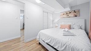 A modern bedroom with a large bed, white walls, and a wooden floor. - Charming 1-bed basement, WI-fi & Pull Out Sofa (Barrie)