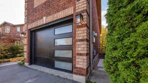 A modern garage with a large black door, brick walls, and a well-maintained hedge. - Charming 1-bed basement, WI-fi & Pull Out Sofa (Barrie)