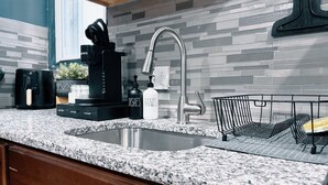 A kitchen with a granite countertop, a stainless steel sink, a coffee maker, a dish soap bottle, and a black knife block. - The Cozy Getaway Suite (Philadelphia)