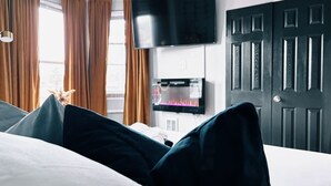 A hotel room with a bed, a flat-screen TV mounted on the wall, a fireplace, and a door. - The Cozy Getaway Suite (Philadelphia)