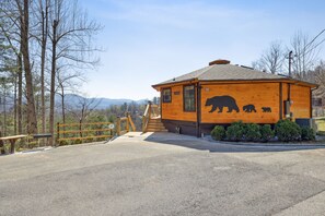 Une cabane en bois ornée d’une fresque représentant un ours, avec un escalier et une vue sur les montagnes.