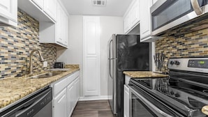 A modern kitchen with white cabinets, a black refrigerator, a stainless steel microwave, and a granite countertop.
