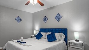 A hotel room with a large bed, blue and white pillows, a nightstand with a lamp, and decorative wall tiles.