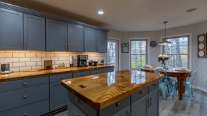A kitchen with grey cabinets, a wooden countertop, and a dining area with a table and chairs.