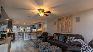 A spacious living room with a dark brown leather sofa, zebra-patterned ottomans, and a ceiling fan.