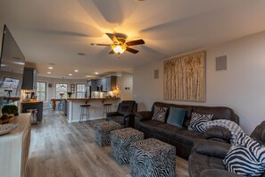 A spacious living room with a dark brown leather sofa, zebra-patterned ottomans, and a ceiling fan.