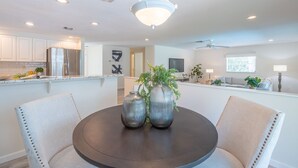 Una cocina moderna con electrodomésticos de acero inoxidable, un comedor con una mesa redonda y sillas, y una sala de estar con un sofá y un televisor.