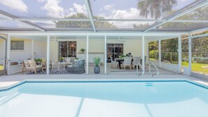 Zona de piscina exterior techada con asientos y una mesa de comedor.