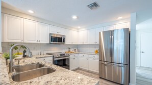 Una cocina moderna con armarios blancos, electrodomésticos de acero inoxidable, encimeras de granito y microondas integrado.