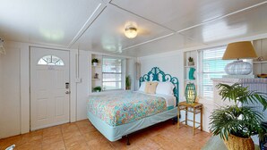 Un dormitorio con cama, una puerta, un ventanal, una mesita de noche y una lámpara.