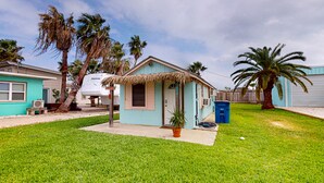 Una pequeña casa de un piso con techo de paja, un porche y una puerta azul.