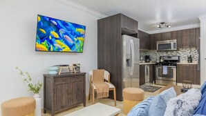 Ein modernes Wohnzimmer mit Flachbildfernseher, einer Couch, einem Couchtisch, einem Schrank und einer Küchenzeile mit Kühlschrank, Mikrowelle und Backofen.