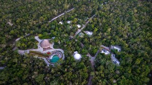Vista aèria d'una zona boscosa amb un edifici circular, una piscina i diverses estructures més petites.