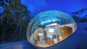 Una estructura esfèrica transparent amb l'interior visible, que conté un llit, una taula i una làmpada.