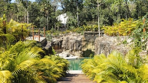 Un camí de fusta que condueix a una piscina envoltada de vegetació abundant i un penya-segat rocos.