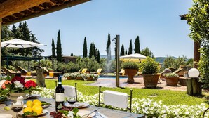 Un espace extérieur aménagé pour les repas, avec une table pour deux, entouré de plantes en pot et offrant une vue sur la piscine et les arbres.