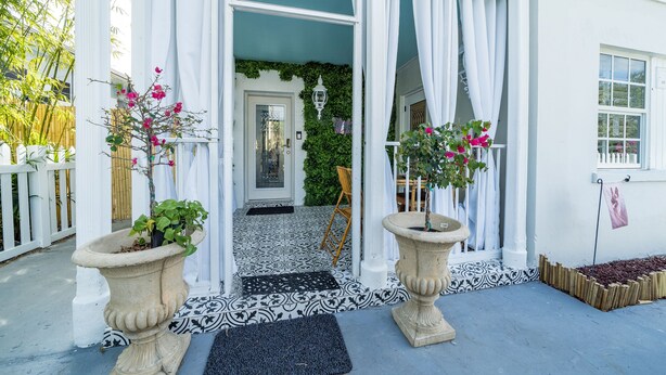 Un edificio bianco con ingresso in pietra, due grandi fioriere con fiori e un recinto in legno.