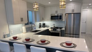 A modern kitchen with white cabinets, stainless steel appliances, and a central island with bar stools. - Modern 2BDRM/2BATH Beachfront Condo in Hermosa (Hermosa Beach)