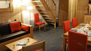 A cozy room with a wooden staircase, a dining table set with plates, glasses, and a kettle, and a sofa with red cushions. - Beautiful apartment for 8 guests with WIFI, pool, TV, terrace and pets allowed (Bourg-saint-maurice)